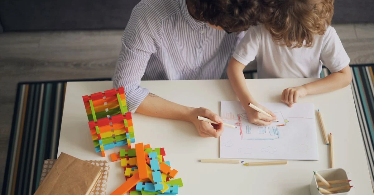 Une mère et son enfant dessinent avec des crayons de couleur à une table, favorisant la créativité et l'apprentissage.