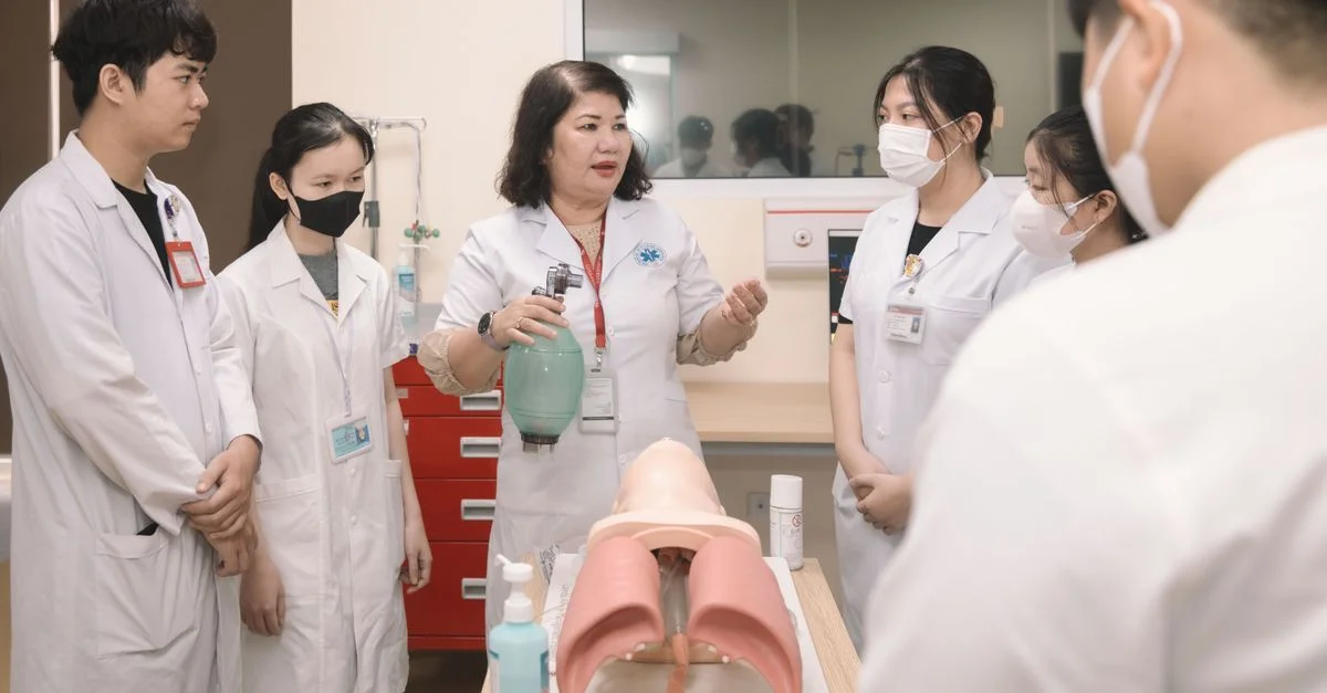 Groupe d'étudiants en médecine pratiquant des compétences avec un mannequin d'entraînement dans une salle de classe.