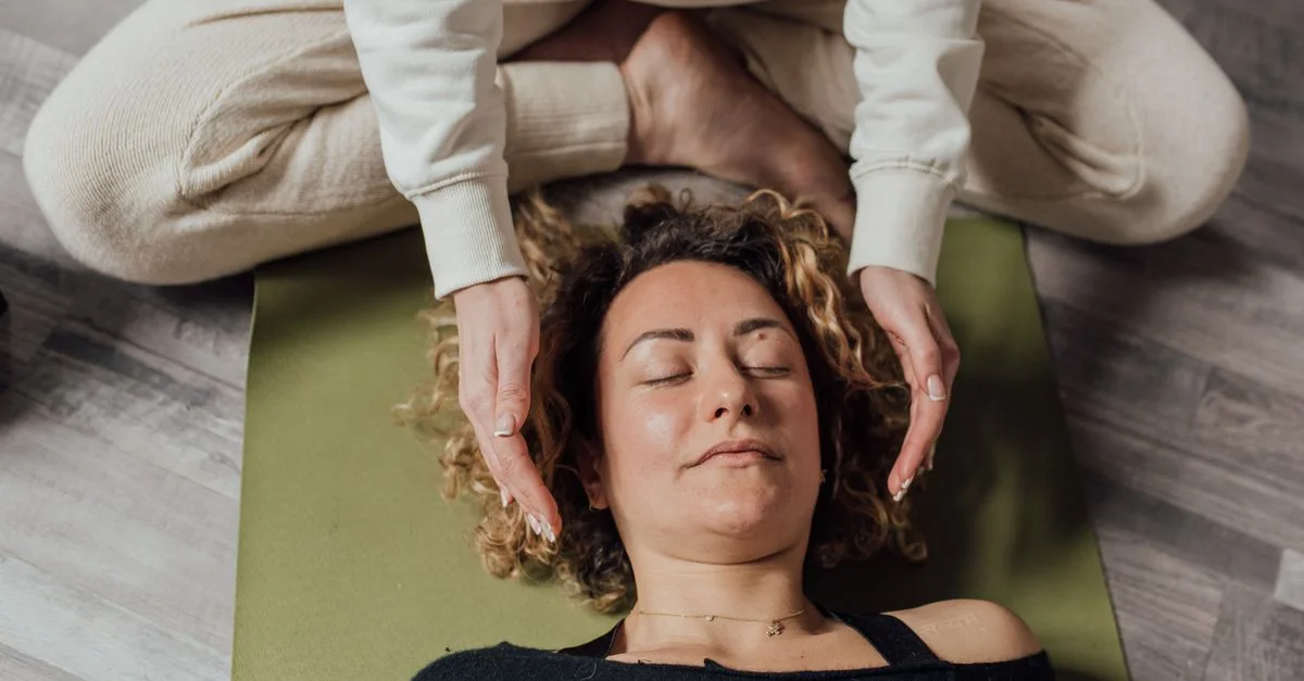 Une femme recevant une thérapie Reiki relaxante sur un tapis de yoga à l'intérieur.