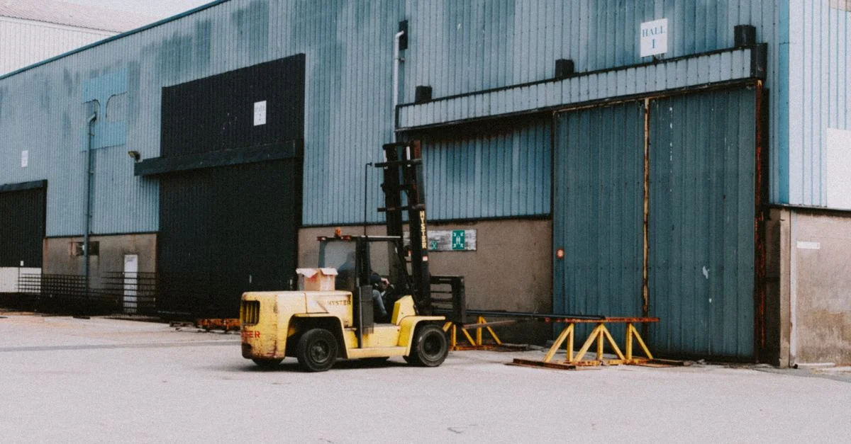 Un chariot élévateur garé devant une zone de chargement d'un entrepôt industriel par une journée ensoleillée.