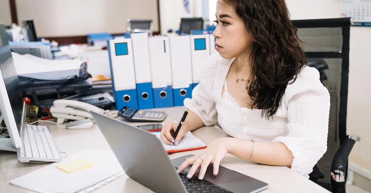 Femme asiatique travaillant attentivement à son bureau avec un ordinateur portable et des documents dans un cadre de bureau organisé.