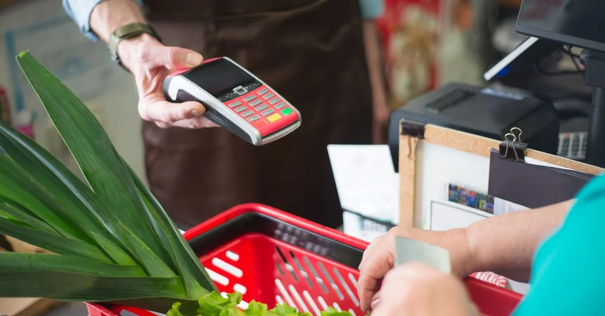 Un client utilisant un moyen de paiement sans contact à la caisse d'un supermarché avec des produits frais.