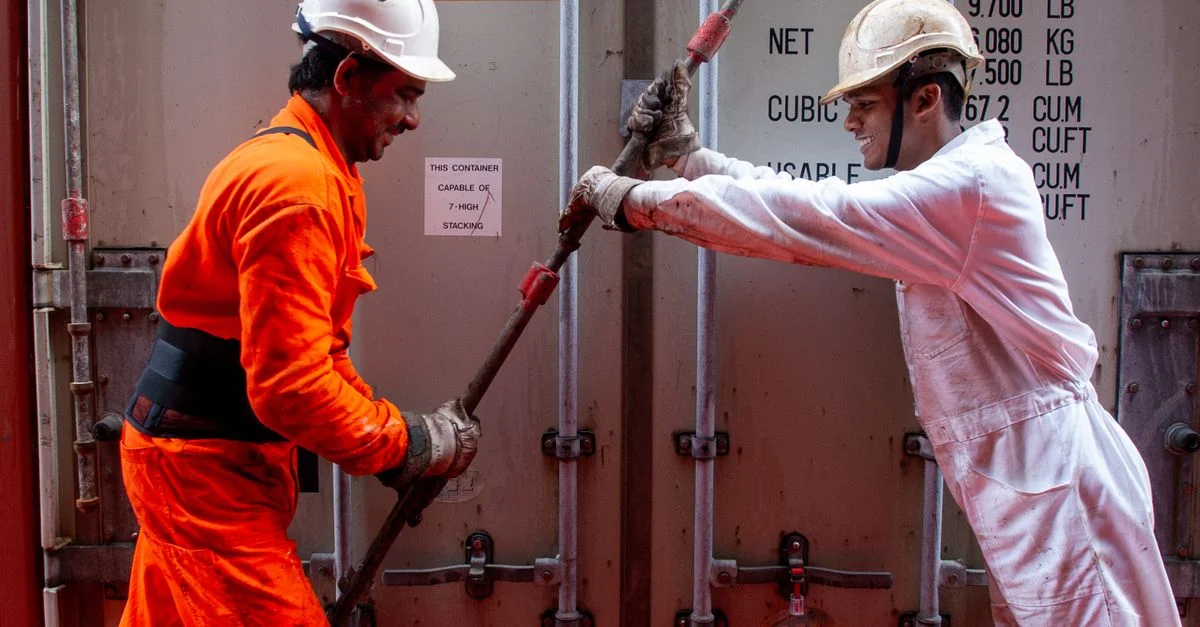 Deux dockers sécurisant un conteneur sur un navire, mettant en avant le travail d'équipe et la sécurité.