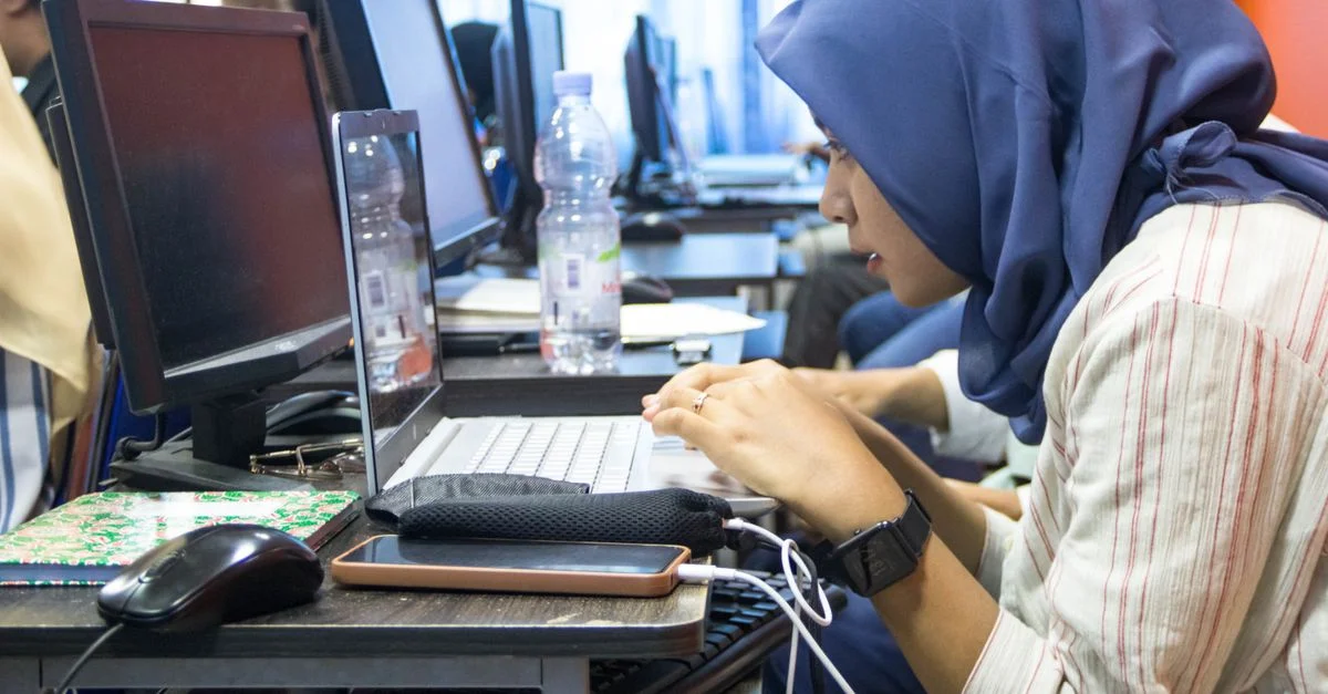 Une jeune femme en hijab utilisant un ordinateur portable dans un cadre de salle de classe d'informatique.
