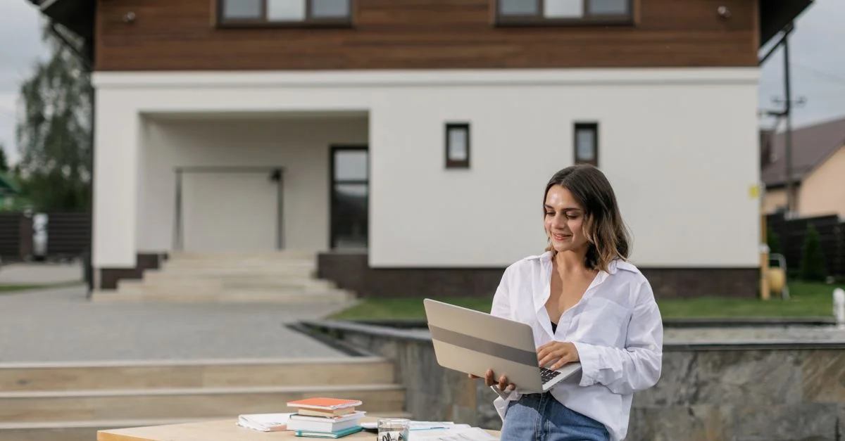 Femme en tenue décontractée utilisant un ordinateur portable à l'extérieur à une table avec des livres.