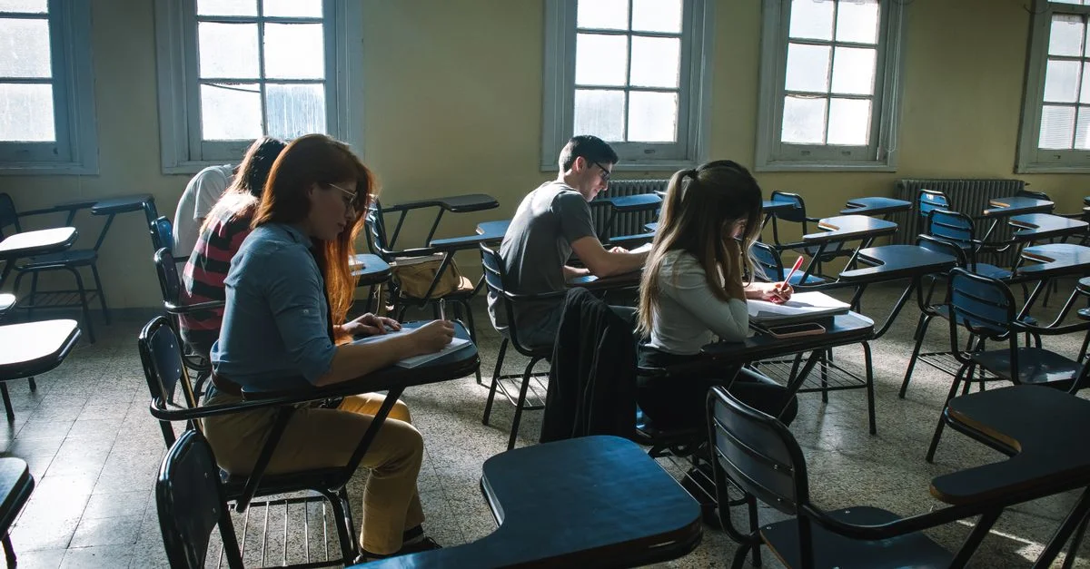 Un groupe d'étudiants concentrés sur un examen dans une salle de classe baignée de soleil.