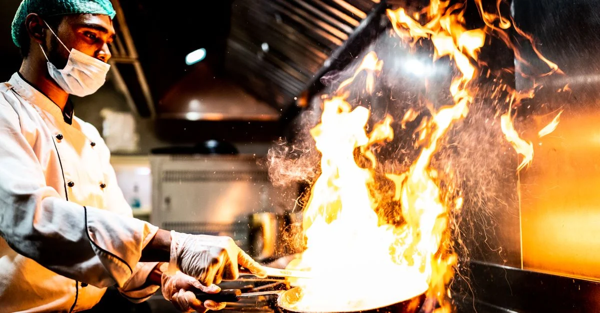 Un chef talentueux réalise une technique de cuisson flambée spectaculaire dans un cadre de cuisine professionnelle.
