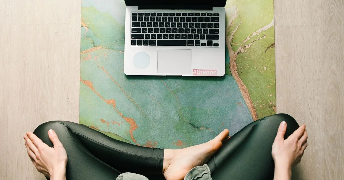 Adulte assise en tailleur sur un tapis de yoga utilisant un ordinateur portable, vue de dessus.