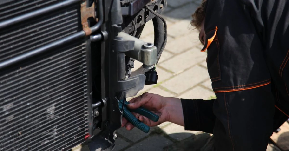 Mécanicien travaillant à la réparation de voiture en plein air avec des outils, se concentrant sur la zone du radiateur du véhicule.
