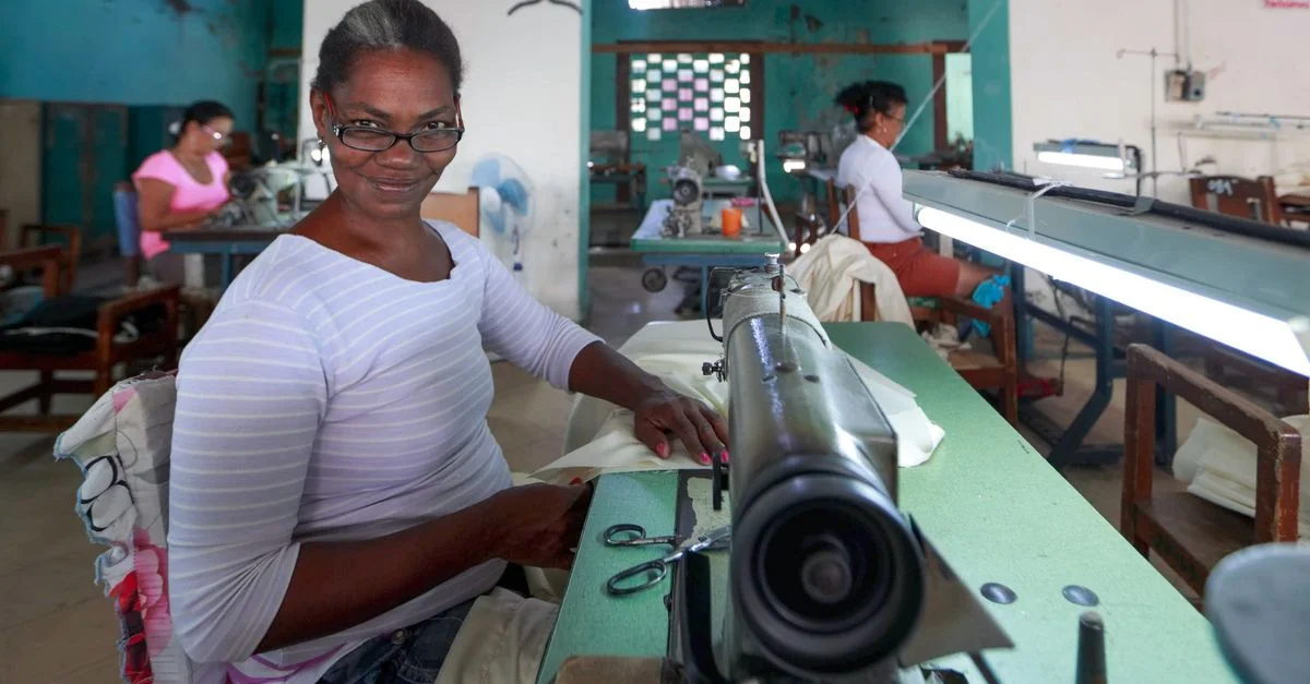 Femme souriante travaillant avec une machine à coudre dans un atelier animé.