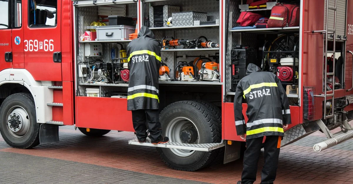Pompiers en uniforme organisant l'équipement sur un camion de pompier avec des compartiments ouverts dans un cadre urbain.