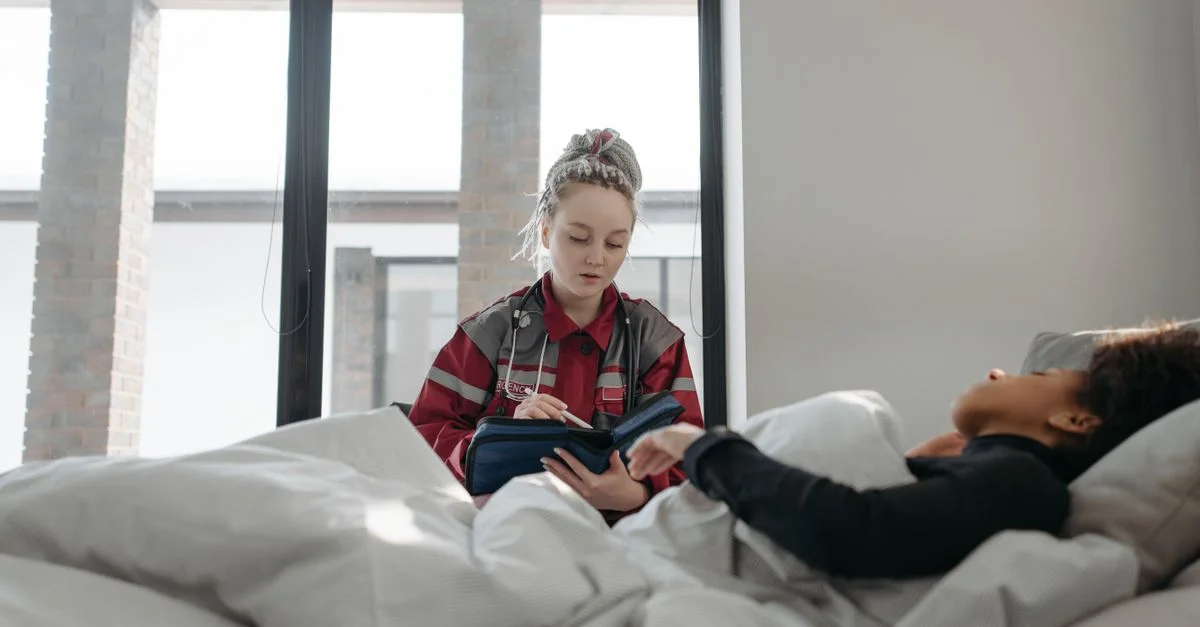 Un professionnel de la santé prend des notes tout en s'occupant d'une patiente au lit, offrant des soins de santé à domicile.