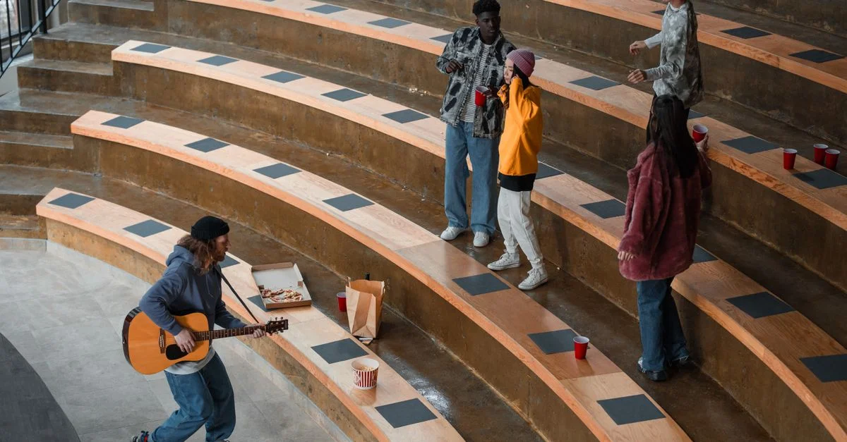 Groupe d'amis dansant et jouant de la guitare, profitant de la convivialité dans un cadre d'amphithéâtre.
