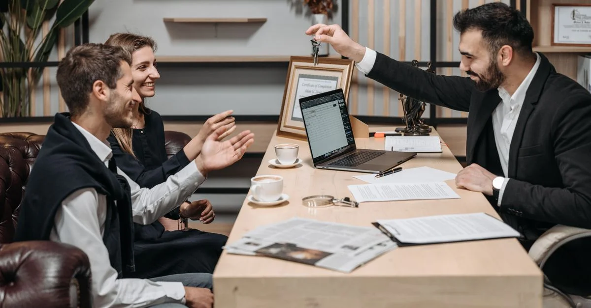 Professionnel des affaires remettant des clés à des clients souriants à un bureau lors d'une consultation.