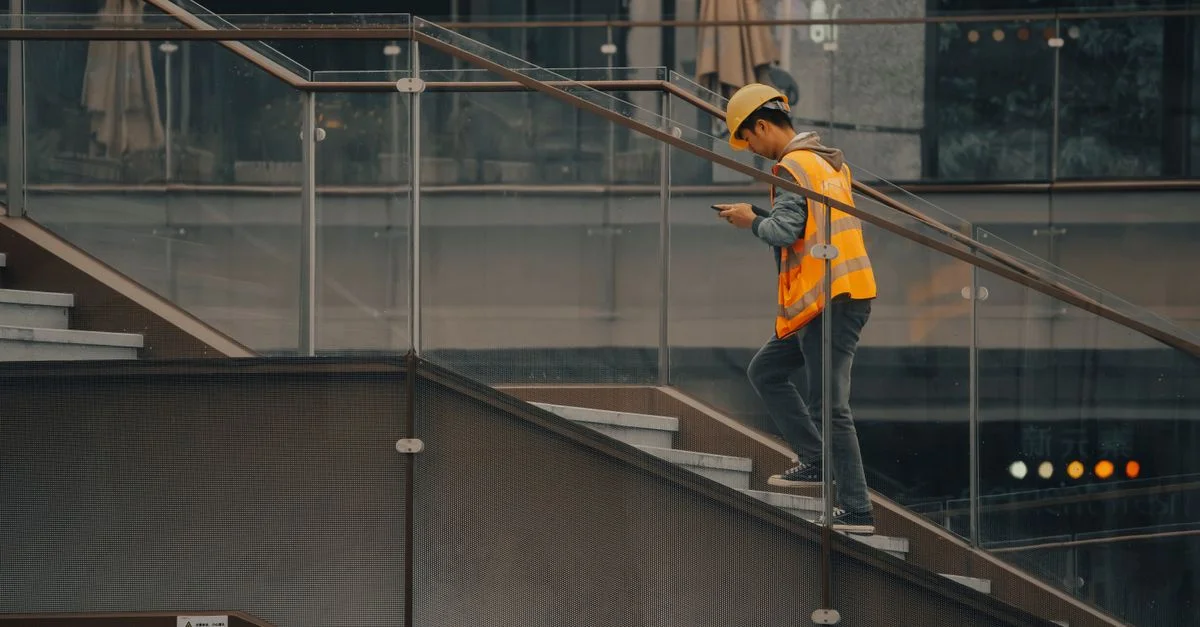 Un travailleur de construction adulte portant un casque de sécurité et un gilet montant des escaliers à l'intérieur d'un bâtiment.