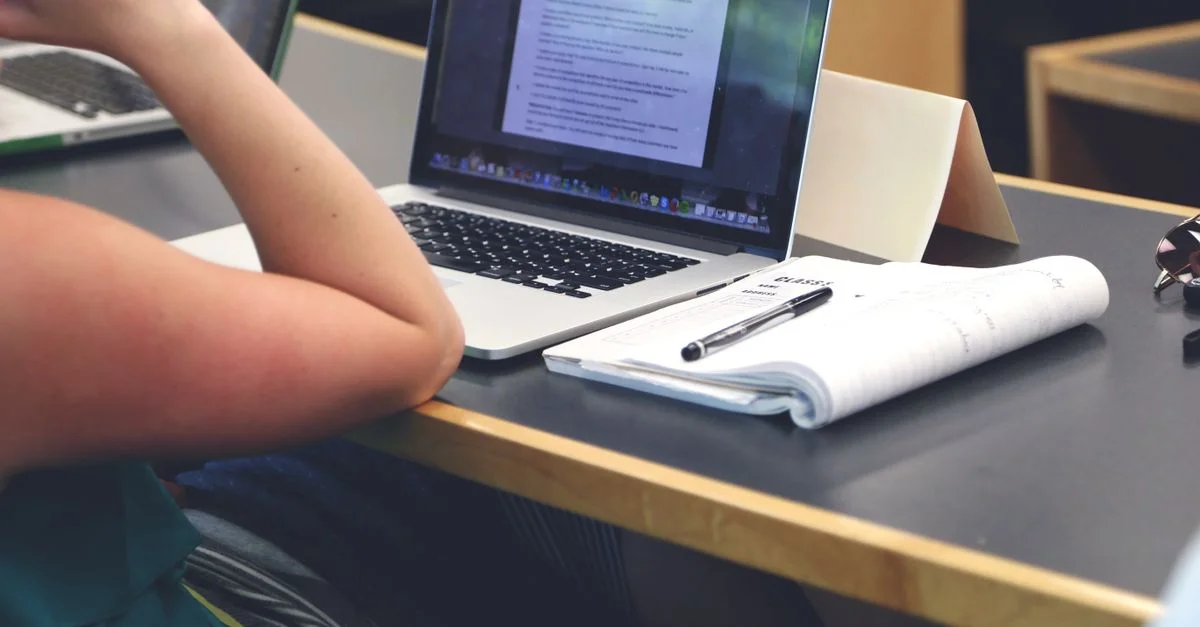 Un étudiant dans une salle de classe utilisant un ordinateur portable et prenant des notes dans un carnet.