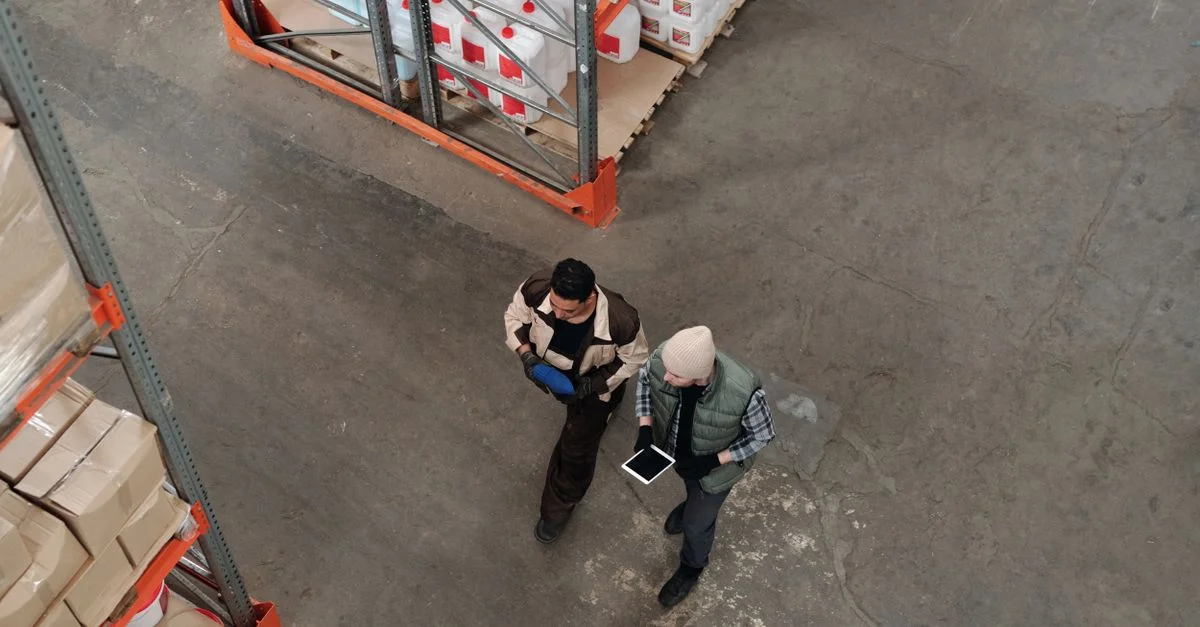 Deux travailleurs discutant de l'inventaire dans un entrepôt, utilisant une tablette numérique pour la coordination.