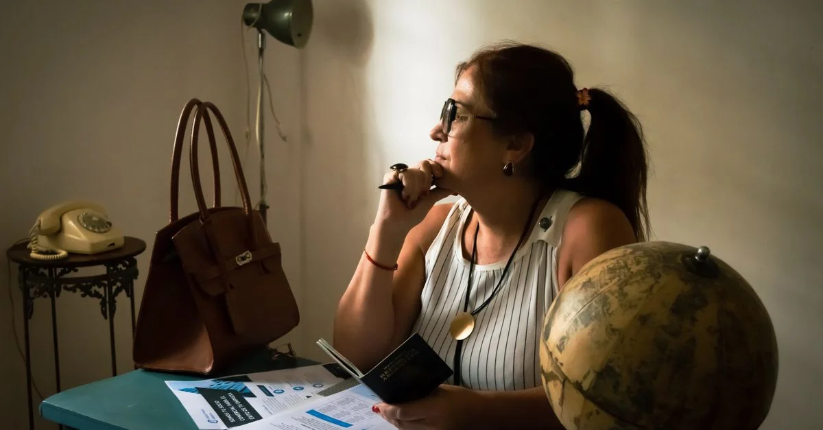 Une femme dans son bureau à domicile, songeuse à un voyage, des documents et un globe terrestre à la main.
