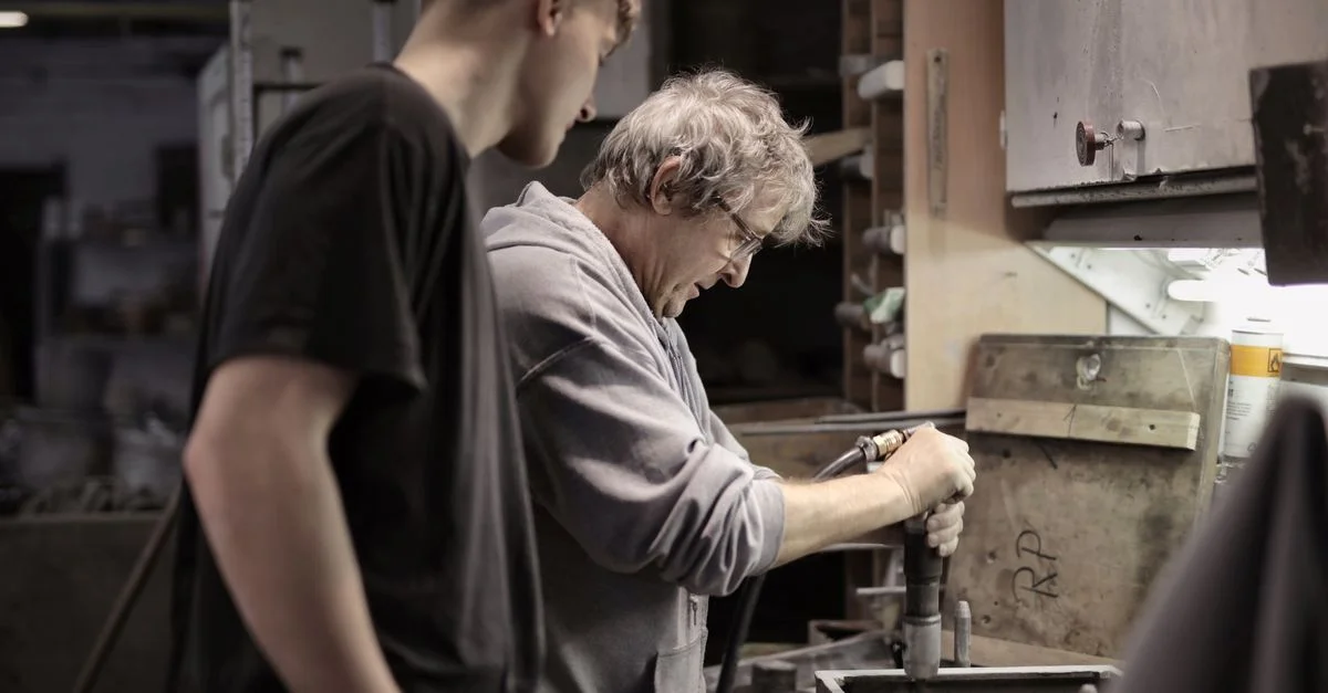 Un artisan démontre des techniques de métallurgie à un jeune apprenti dans un atelier.