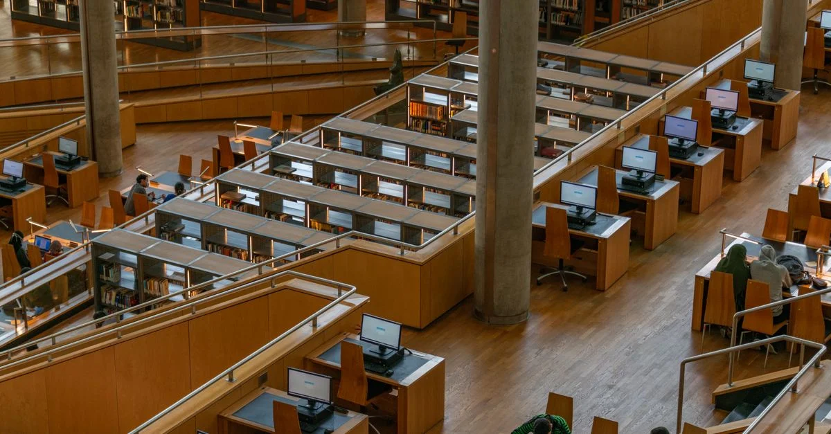 Vue intérieure spacieuse de la Bibliotheca Alexandrina présentant des zones d'étude en bois et des ordinateurs.
