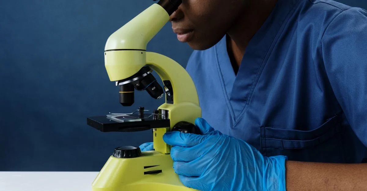 Scientifique en blouse utilisant un microscope dans un laboratoire.