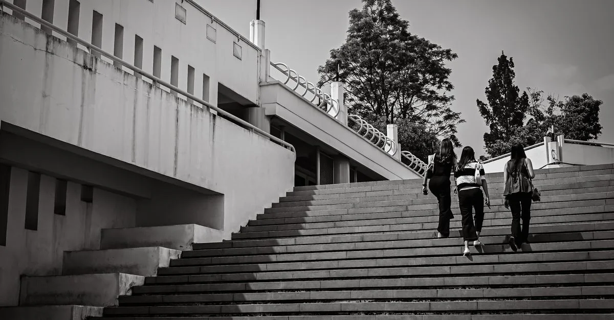 Photo en noir et blanc d'une architecture de campus moderne avec des personnes montant des escaliers à l'extérieur.