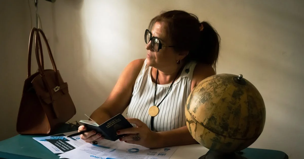 Une femme assise à l'intérieur examine des documents de voyage à côté d'un globe terrestre, ce qui suggère qu'elle prépare un voyage.