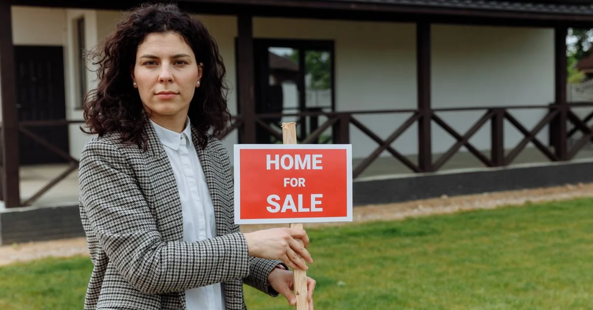 Agent immobilier confiant avec une affiche de vente devant une maison.