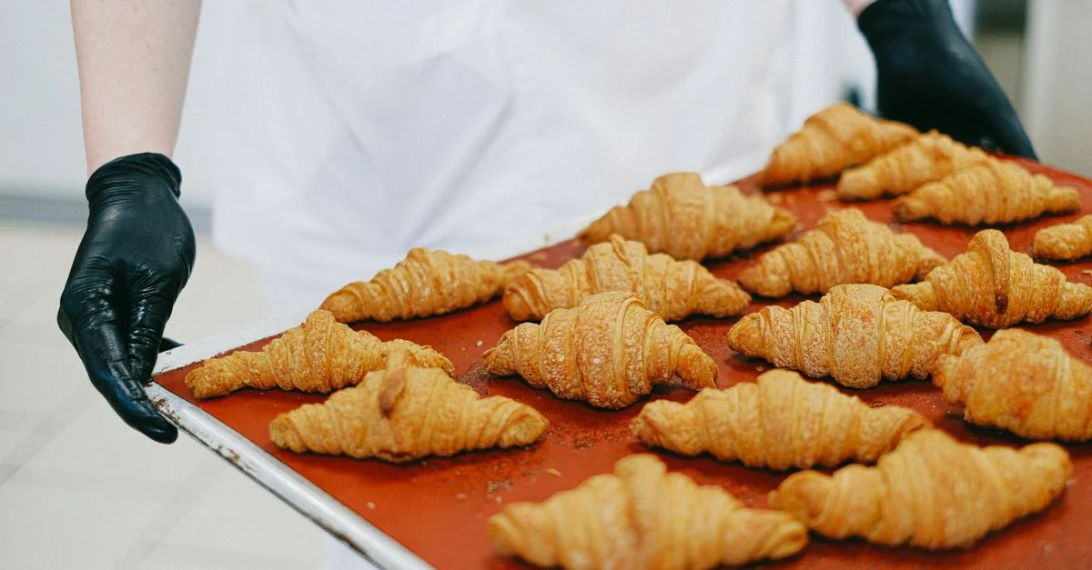 Un boulanger présente des croissants fraîchement cuits sur un plateau, prêts à être servis.