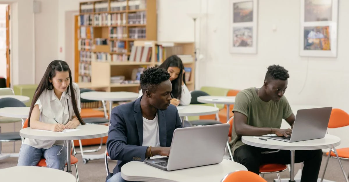 Étudiants concentrés sur des ordinateurs portables et des notes dans une salle de classe lumineuse.