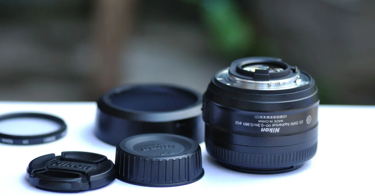 Objectif de caméra DSLR avec bouchons et accessoires exposés sur une surface blanche.
