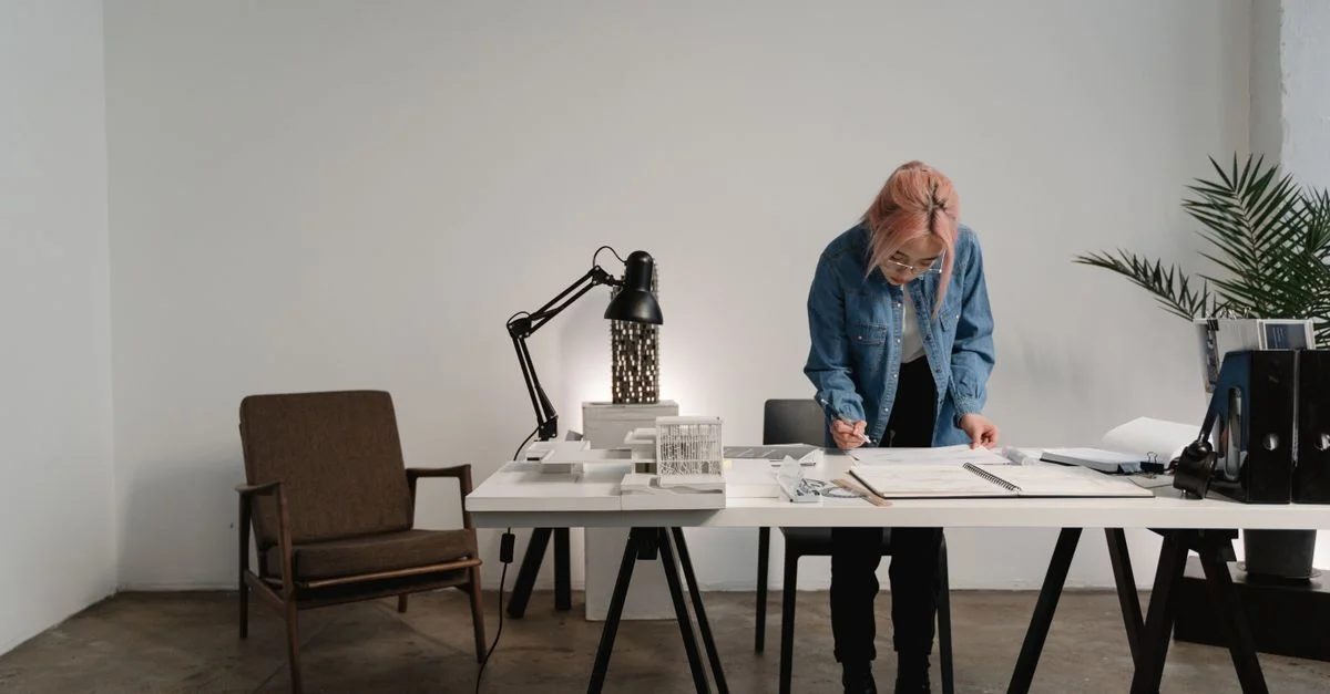 Une personne aux cheveux roses travaillant sur des plans architecturaux dans un bureau moderne.