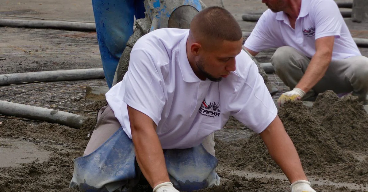 Des ouvriers du bâtiment nivellent avec expertise le béton frais pour obtenir une finition lisse sur un chantier.