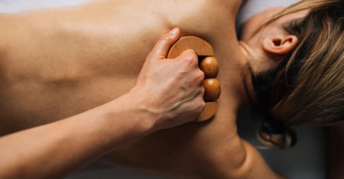 Femme recevant un massage relaxant du dos avec un outil en bois dans un cadre intérieur serein.