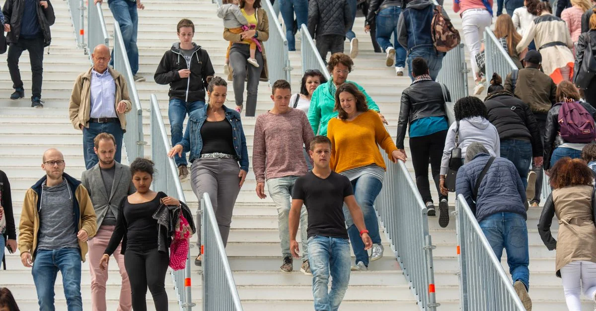 Une foule diversifiée de personnes descendant des escaliers dans un environnement urbain animé, illustrant la vie quotidienne.