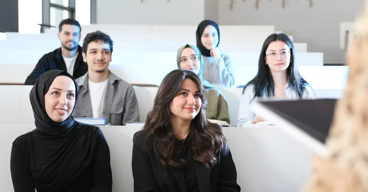 Groupe diversifié d'étudiants écoutant attentivement dans un amphithéâtre universitaire.