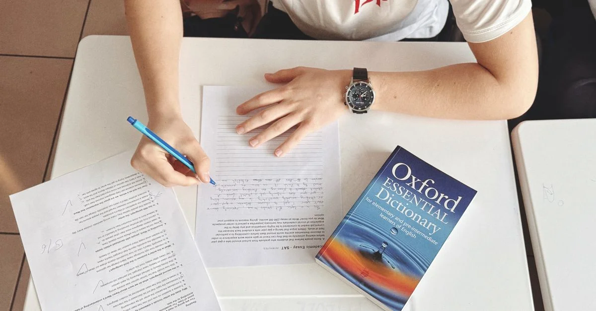 Test d'écriture d'un élève à l'aide de papier et d'un dictionnaire Oxford sur un bureau en classe
