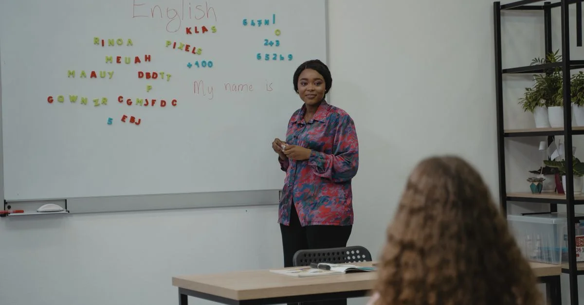Une enseignante expliquant des concepts d'anglais à un étudiant dans une salle de classe avec un tableau blanc.