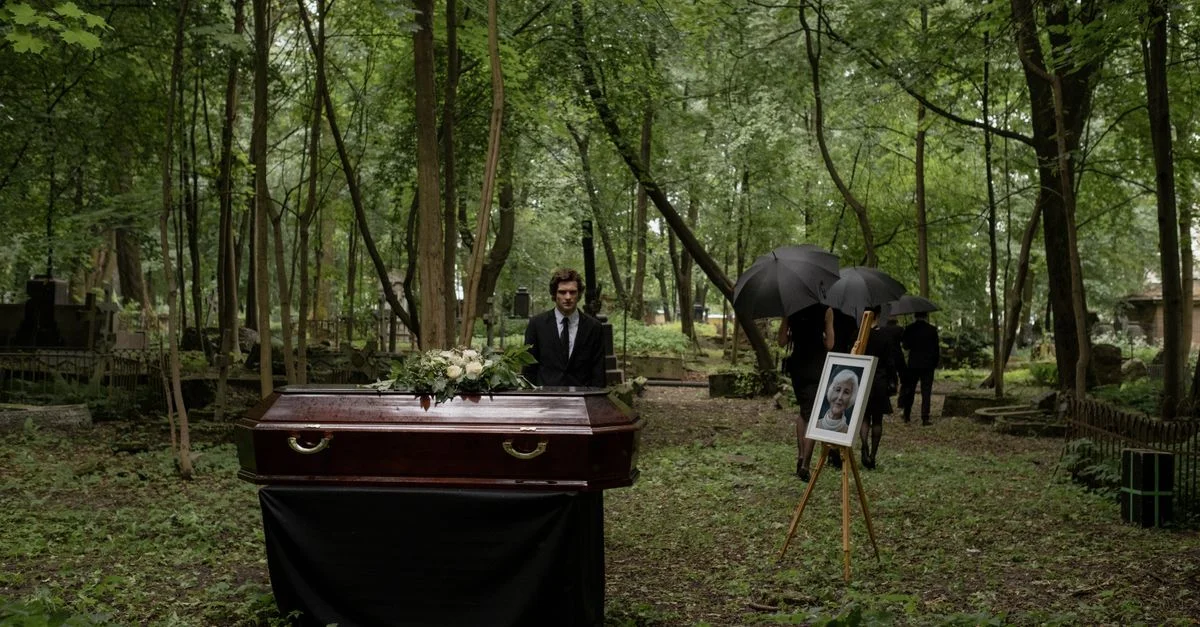 Une cérémonie funéraire dans un cimetière boisé avec un cercueil en bois et des endeuillés.