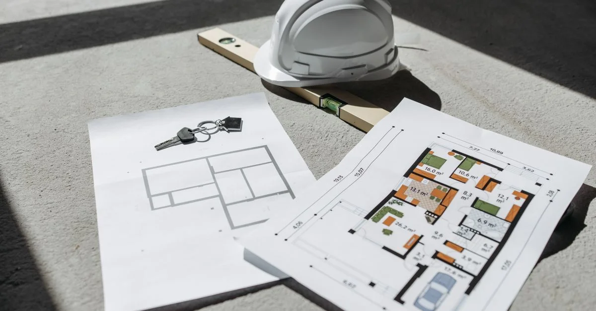 Plans architecturaux avec casque et clés sur un sol ensoleillé, parfaits pour des thèmes immobiliers ou de construction.