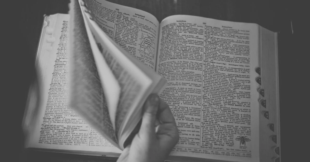 Un gros plan en noir et blanc d'une main feuilletant un dictionnaire ouvert.