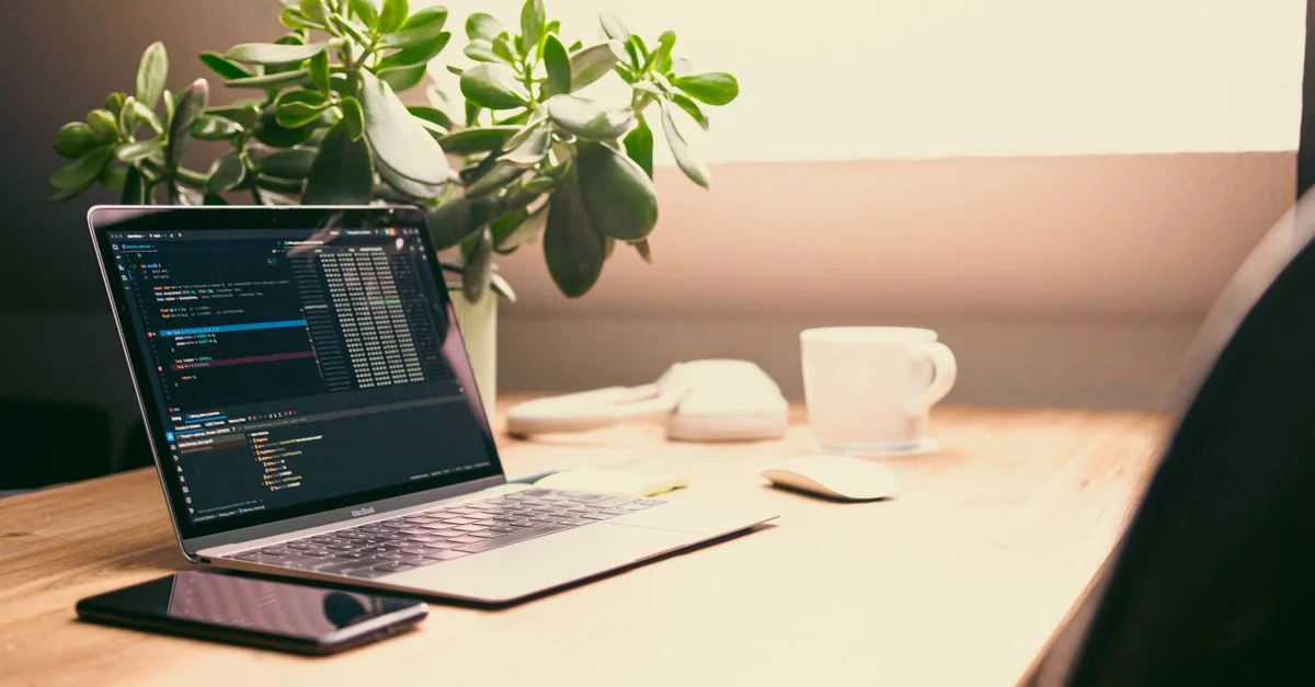 Configuration de bureau à domicile confortable avec ordinateur portable, tablette et plante, idéale pour le travail à domicile.