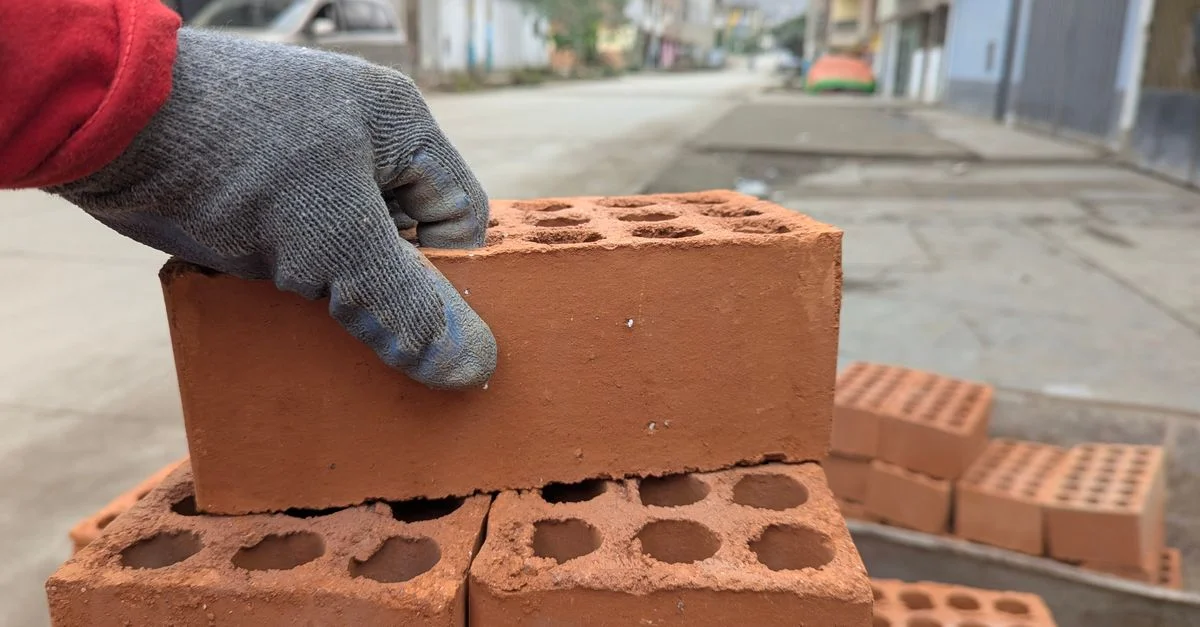 Un travailleur avec un gant empilant des briques sur un chantier de rue.